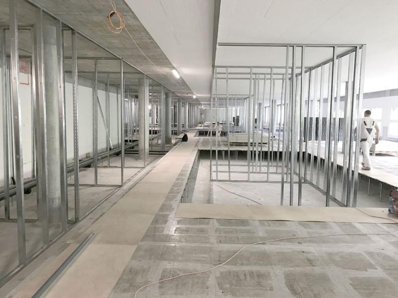 Leerer Büroflur mit Glastrennwänden und Betonboden in einem Rohbauzustand.