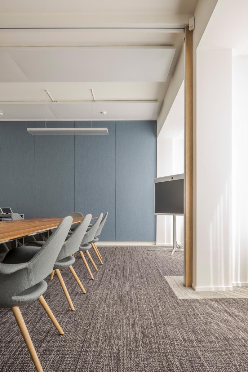 Moderner Konferenzraum mit blauer Wand, Holztisch, grauen Stühlen und Betondecke.