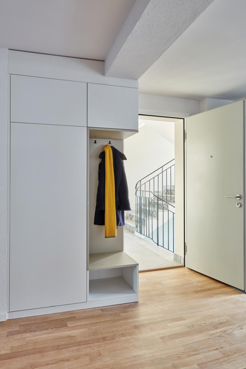 Offene Garderobe mit weißen Schranktüren und gelber Jacke an der Garderobe in einem Wohnflur.
