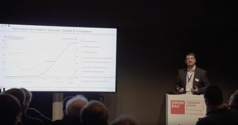 Hannes Reichel präsentiert an einem Podium während der Swissbau 2020 ein Diagramm zur Marktentwicklung.