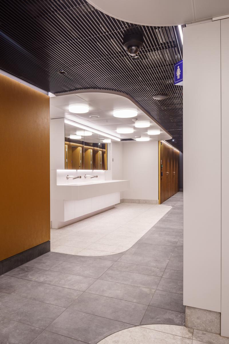 Empfangsbereich eines Hygienecenters mit weißem Tresen, goldfarbenen Türen und strukturierter schwarzer Decke.