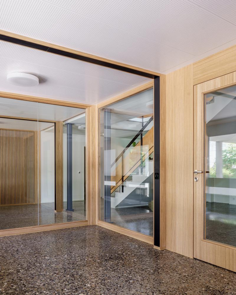 Eingangshalle eines umgebauten Gebäudes mit Holzverkleidung, Glastüren und Betonboden.
