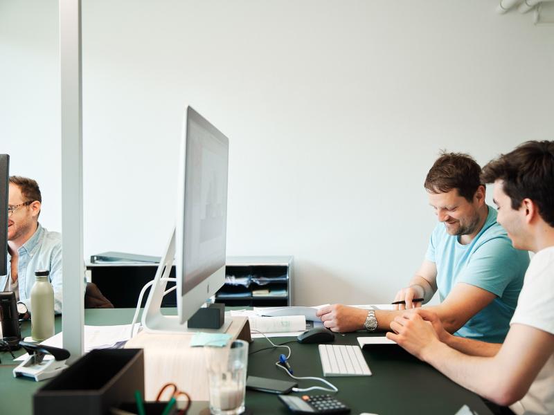 Vier Personen sitzen an einem Schreibtisch vor einem Monitor in einem Büro.