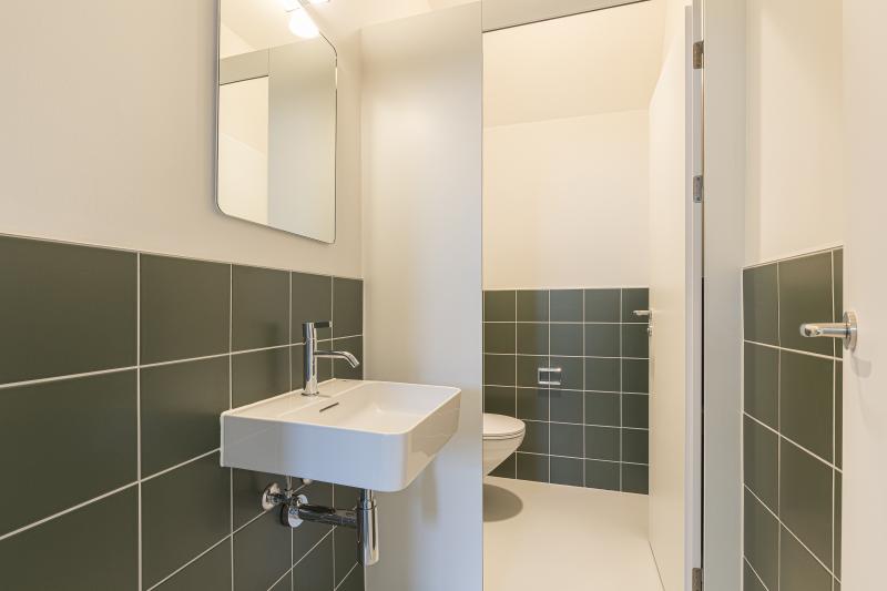 Modernes Badezimmer mit grünen Wandfliesen und weißem Waschbecken am Bahnhof Basel SBB Westflügel.