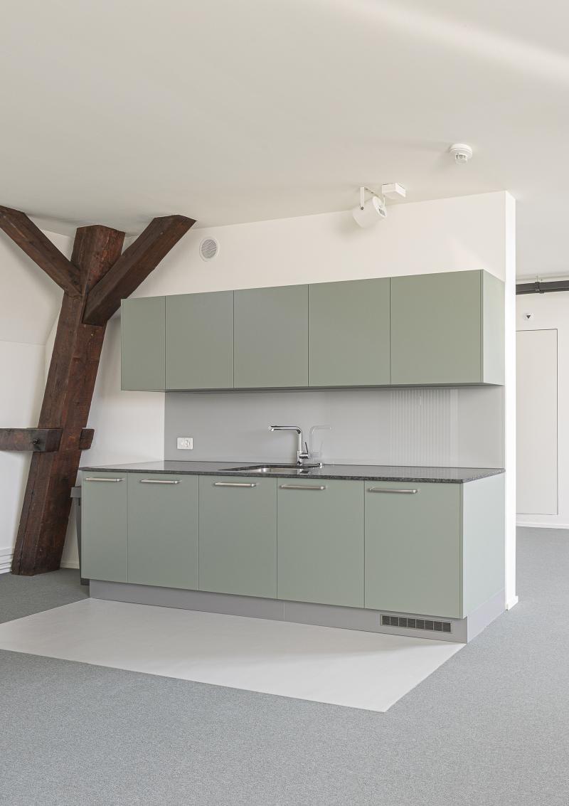 Modernisiertes Bürogeschoss mit grünen Küchenmöbeln und exponierten Holzbalken am Bahnhof Basel SBB.