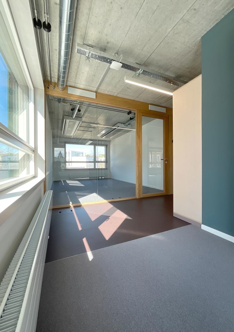 Leerer Büroraum mit Betondecke, Holztüren und grauem Bodenbelag im Hochhaus Hoch3 der Genossenschaft ABZ.