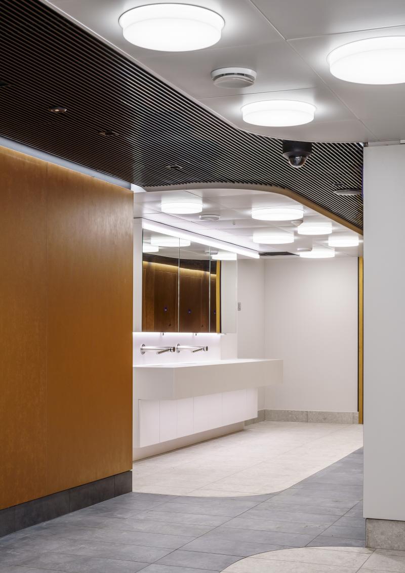 Sanitärbereich mit weissen Waschbecken, schwarzer Deckenverkleidung und runder Beleuchtung im Hygienecenter des Zürcher Hauptbahnhofs.