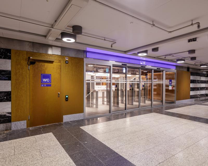 Eingang zum Hygienecenter im Zwischengeschoss des Zürcher Hauptbahnhofs mit Holzverkleidung und modernem Glas-Eingangsbereich.
