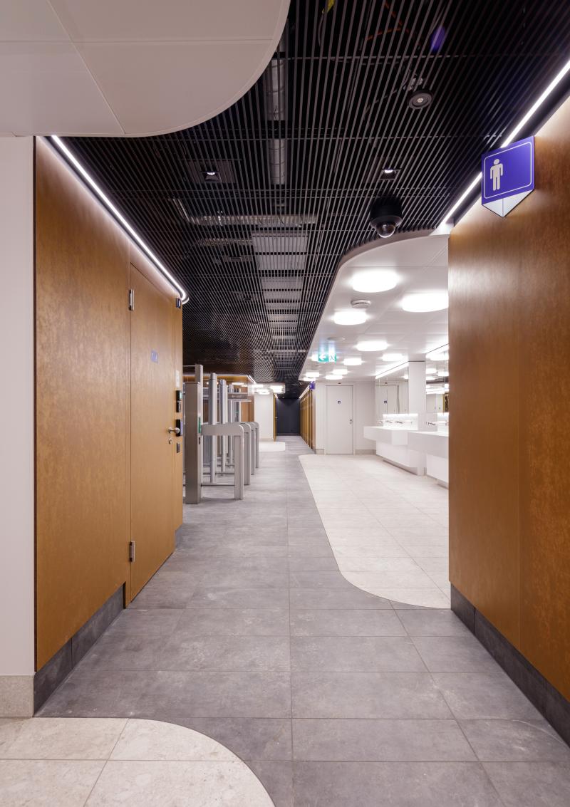 Flur mit geschwungener schwarzer Deckenverkleidung und hölzernen Seitenwänden im Hygienecenter des Zürcher Hauptbahnhofs.