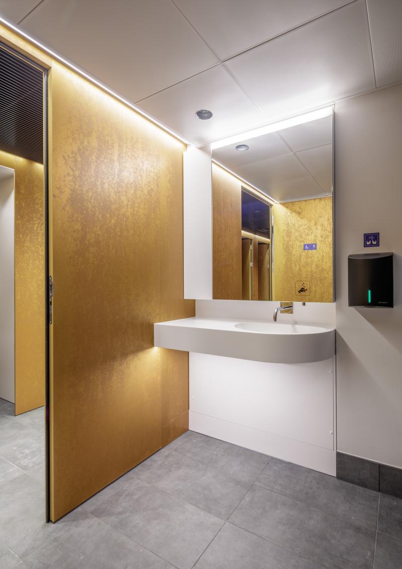 Waschbereich mit goldfarbenen Türen und weißem Waschbecken im Hygienecenter des Zürcher Hauptbahnhofs.