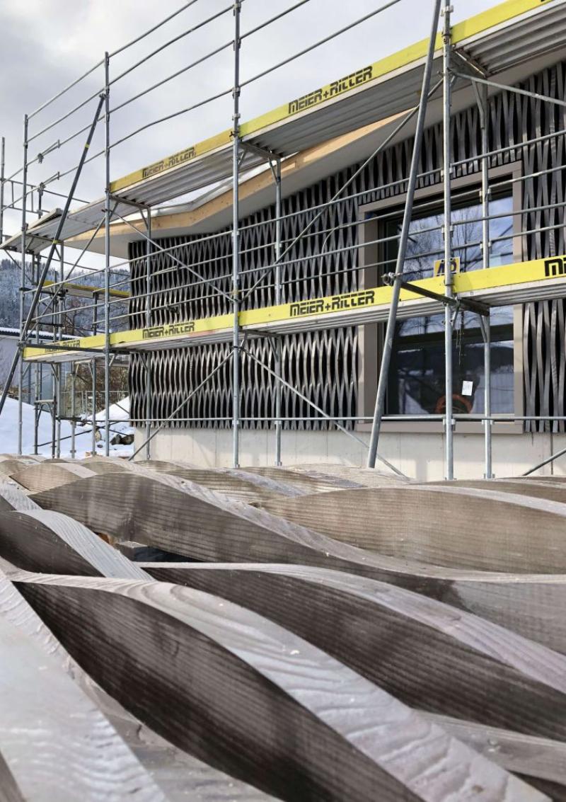 Baustelle des Doppelkindergartens Werd in Adliswil mit Holzfassade unter gelben Schutzgerüsten.