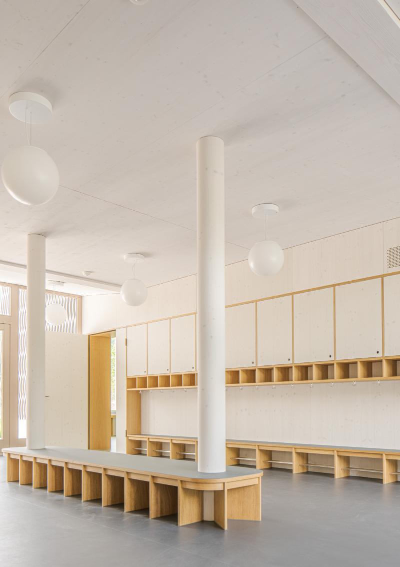 Innenraum des Doppelkindergartens Werd in Adliswil mit Holzregalen und zentralem Pfeiler.