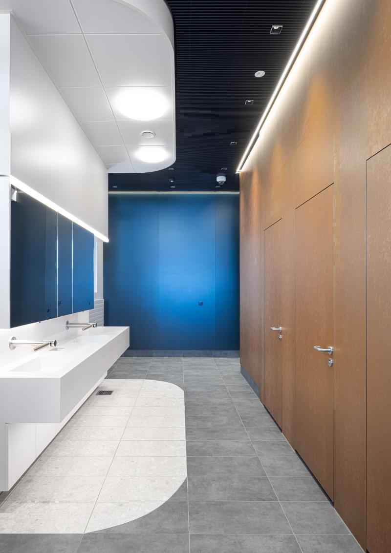 Moderner Sanitärbereich mit weißem Waschbecken, blauer Wand und holzverkleideten Türen in den Kundenbereichen der SBB.