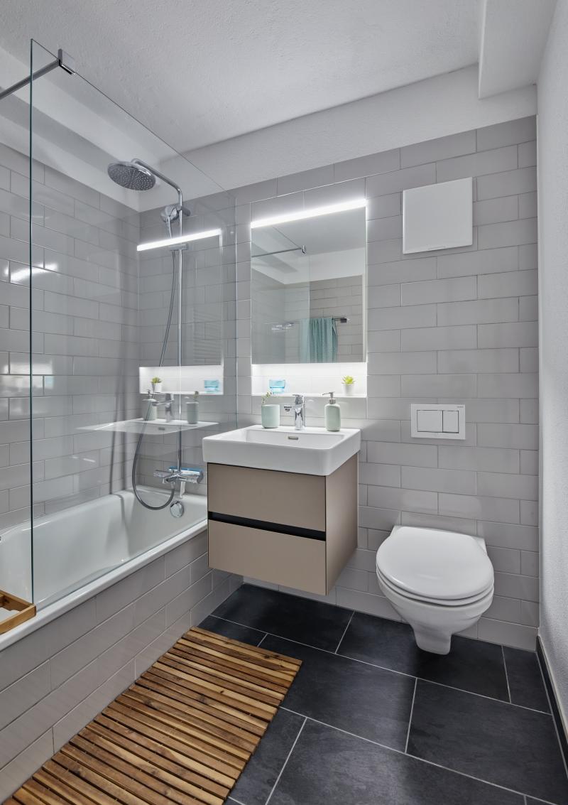 Badezimmer mit grauem Fliesenwerk, Dusche, Doppelwaschbecken und Toilette in einem sanierten Mehrfamilienhaus in der Luzerner Innenstadt.