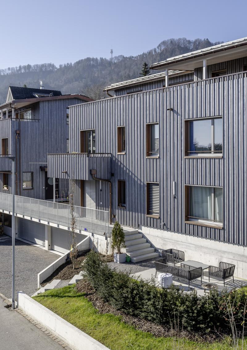 Zwei Mehrfamilienhäuser mit Holzfassade und Sichtbetonsockel an einem Hang in Adliswil.