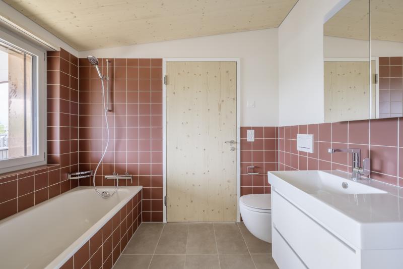 Badezimmer mit roten Fliesen und weißem Waschbecken im Mehrfamilienhaus Leimbachstrasse in Adliswil.