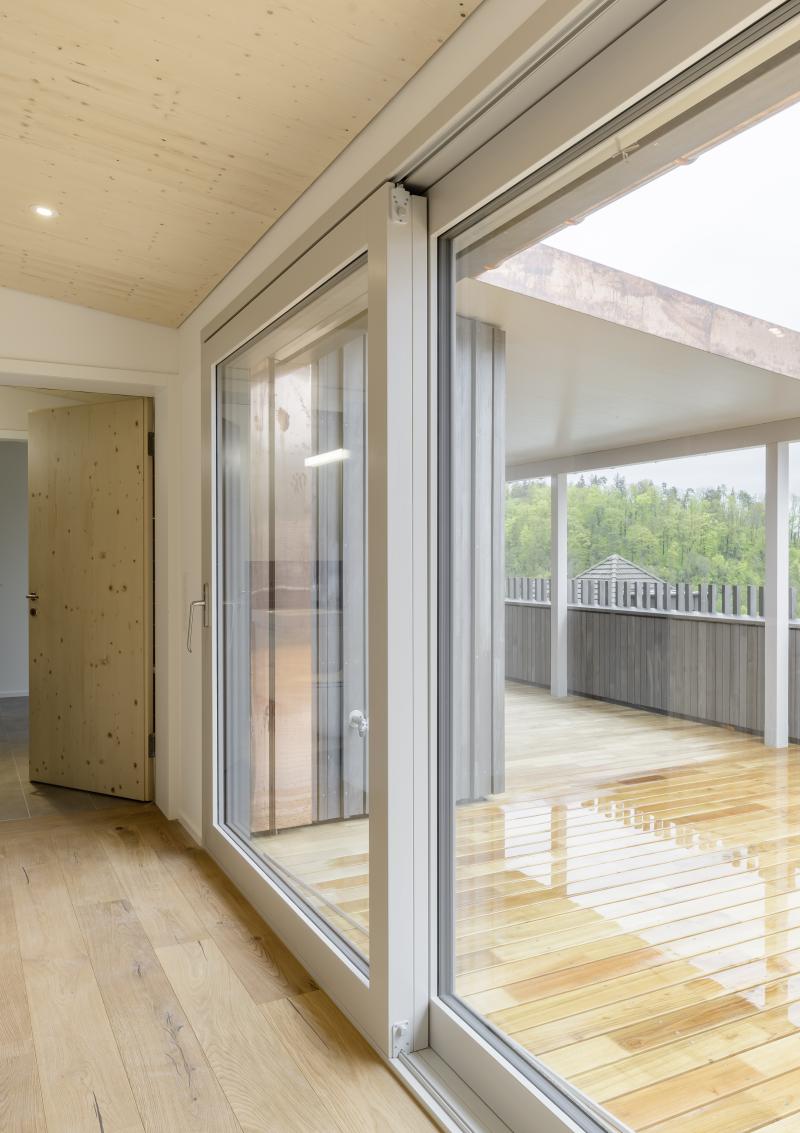 Balkon und Wohnbereich eines Mehrfamilienhauses in Adliswil mit Holzfassade und Ausblick ins Grüne.