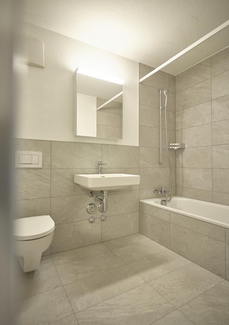 Badezimmer mit Toilette, Waschbecken, Badewanne und Spiegel im sanierten Mehrfamilienhaus Rütistrasse.