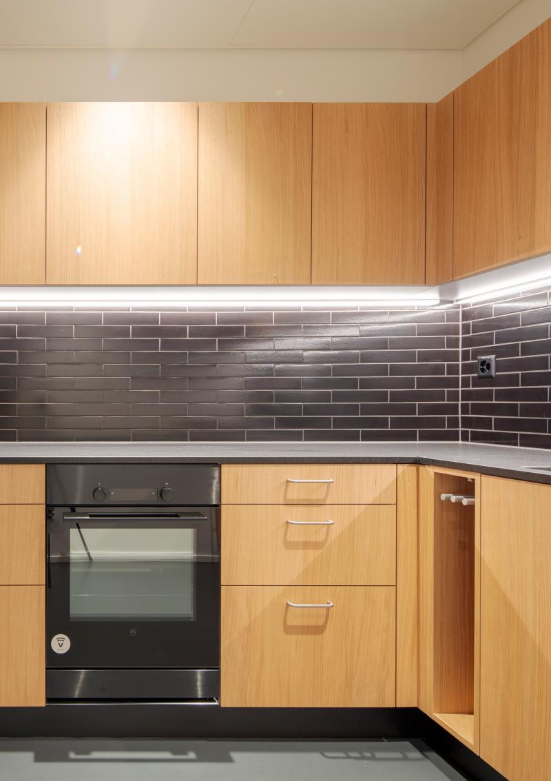 Moderne Küche mit Holzfronten, schwarzem Fliesenspiegel und integriertem Backofen in der internationalen Privatbank Zürich.