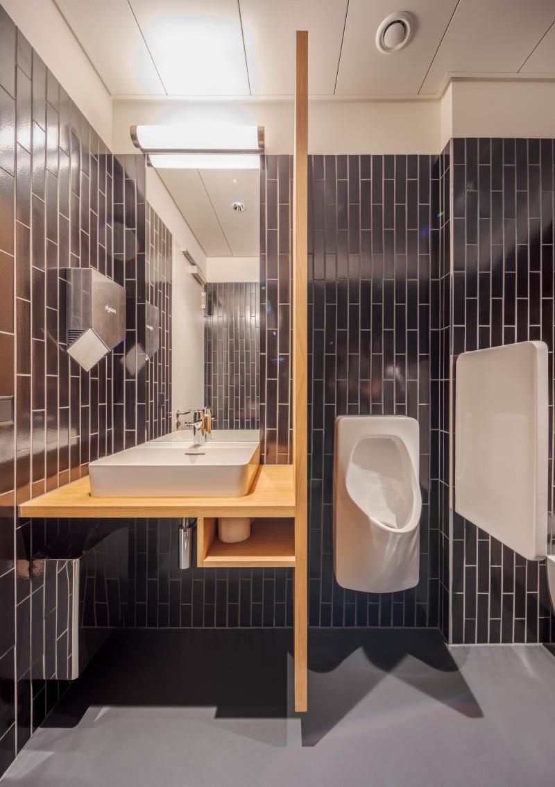 Modernes Badezimmer mit schwarzen Wandfliesen und Holzakzenten in der Privatbank Zürich.