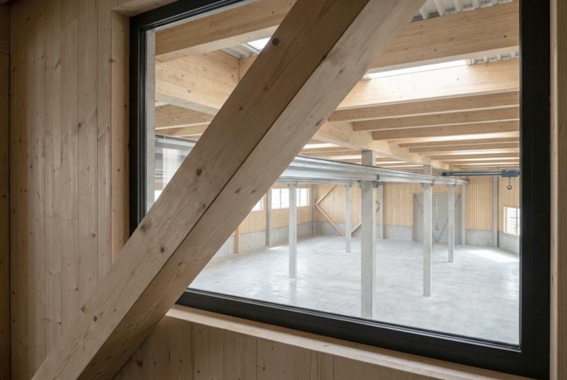 Blick durch ein großes Fenster in die Produktionshalle der Sauter Bachmann AG mit Holzkonstruktion und Betonstützen.