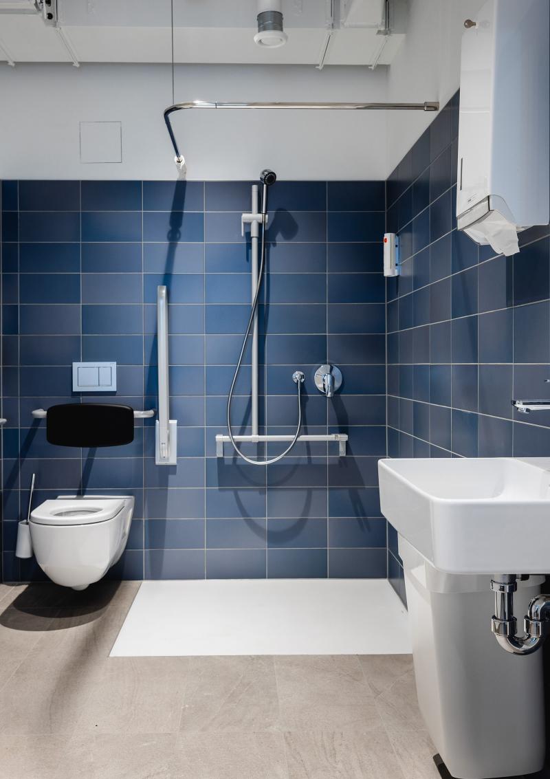 Modernes Badezimmer mit dunkelblauen Fliesen, bodengleicher Dusche und weißem Waschbecken für eine Unternehmensberatung am Raiffeisenplatz in St. Gallen.