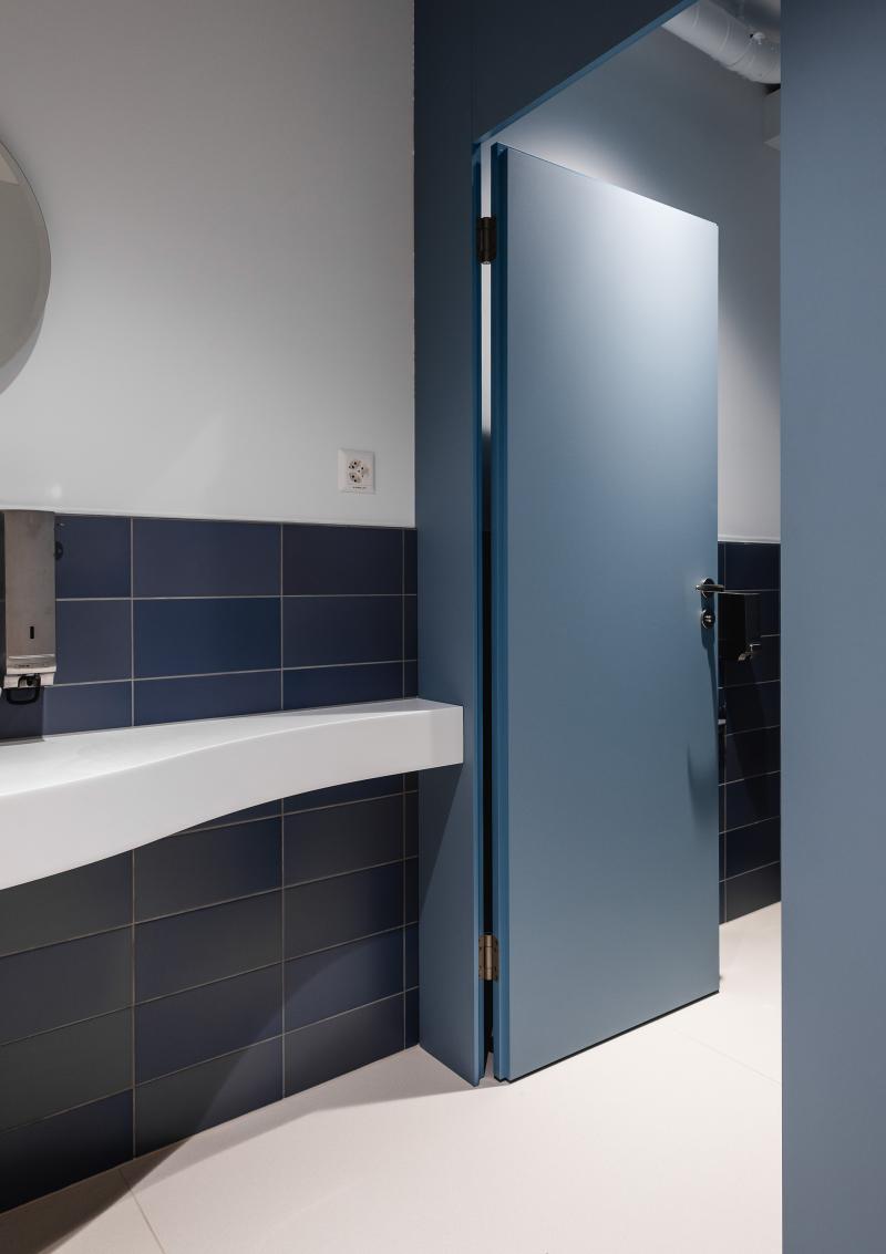 Modernes Badezimmer mit schwarzen Wandfliesen, rundem Spiegel und weißem Waschtisch in einer Unternehmensberatung am Raiffeisenplatz St. Gallen.